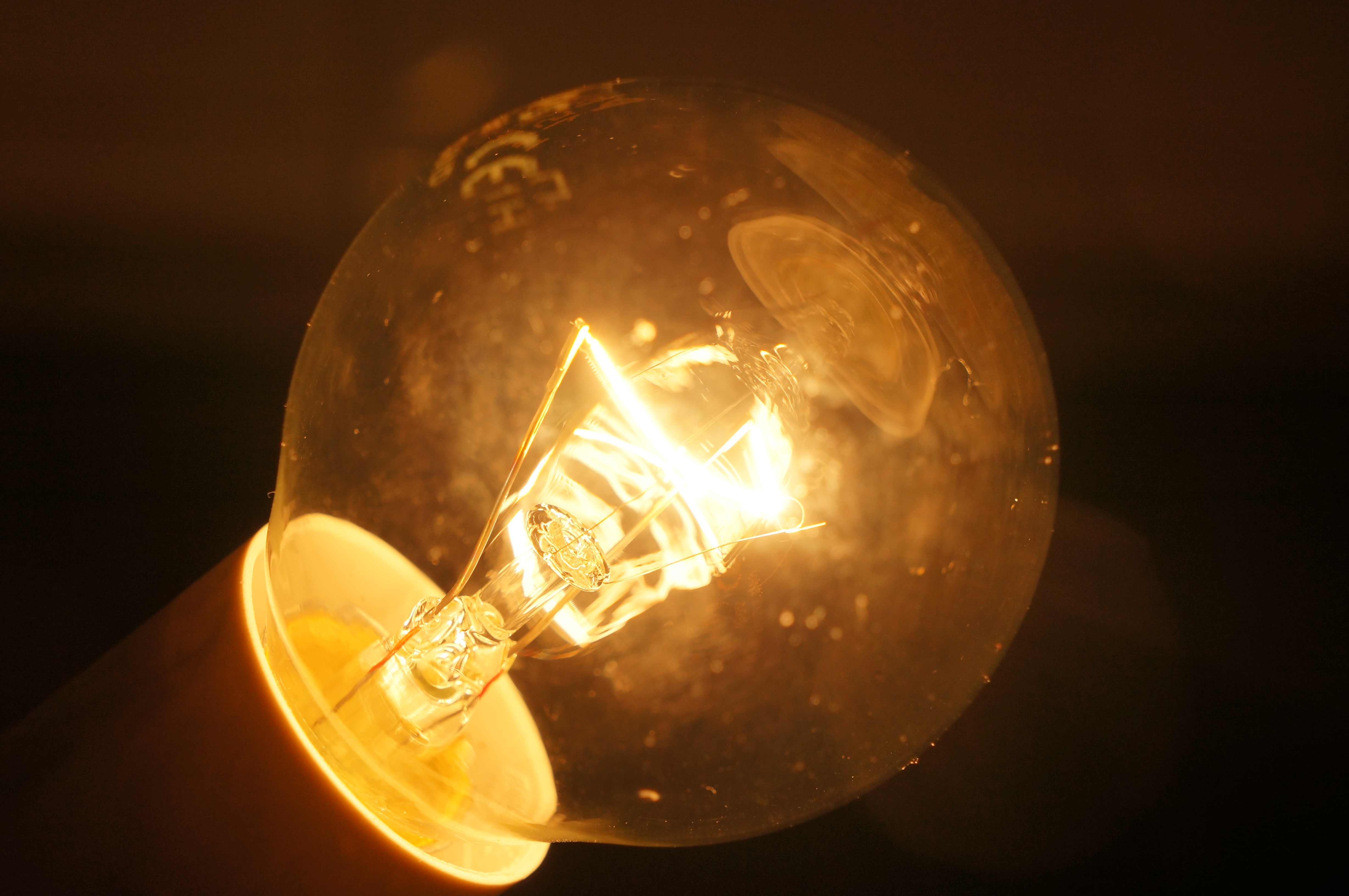 Ampoule à incandescence allumée dans le noir : le filament de tungstène brille d'un blanc incandescent et éclaire l'enveloppe de verre en orange