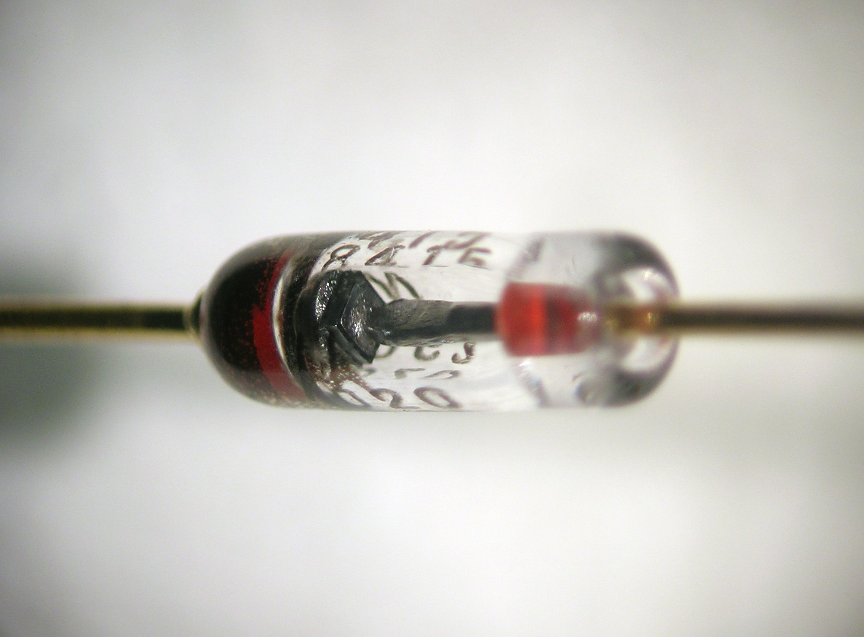 Gros plan sur une diode au silicium : le cristal carré est visible entre les deux pattes, la barre sombre marque la cathode